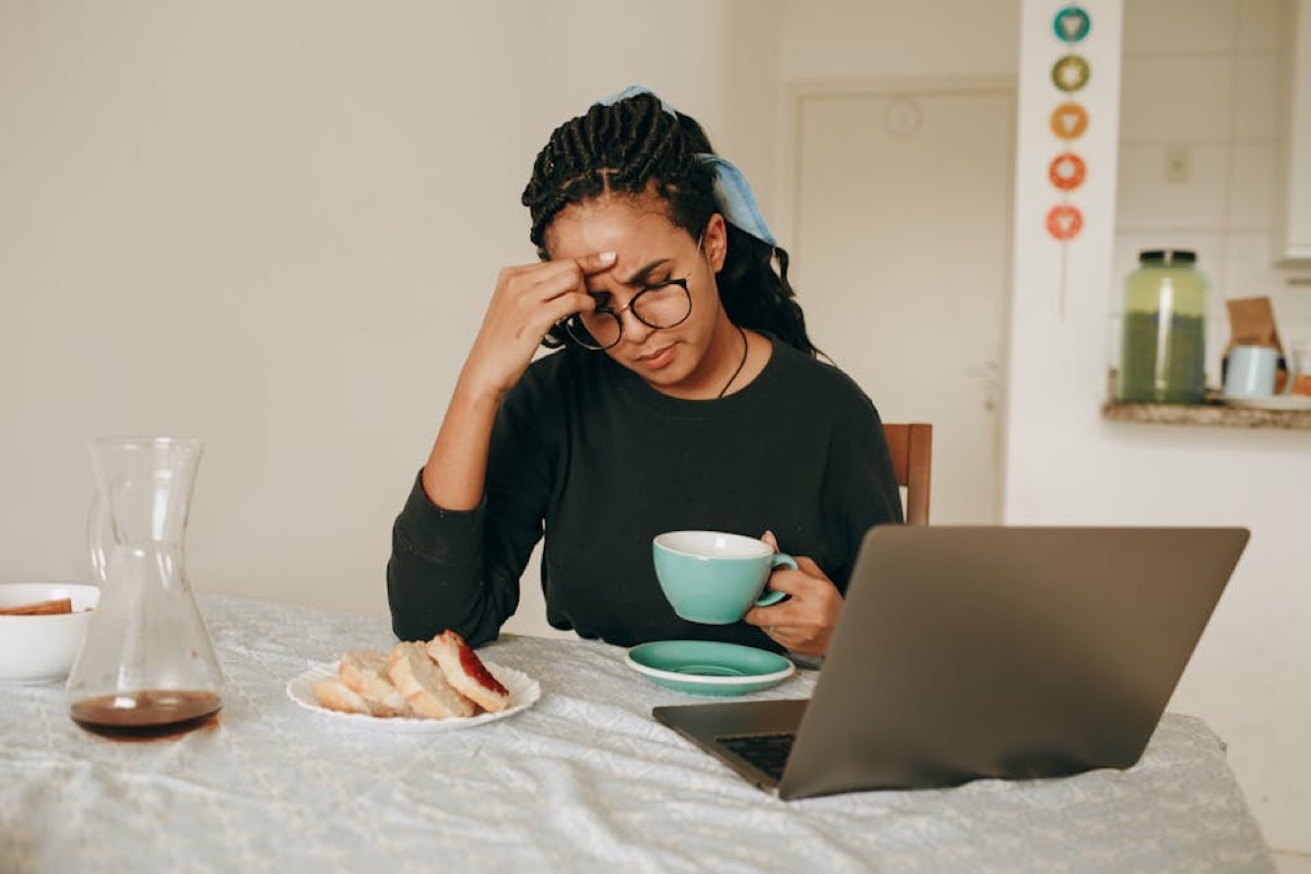 Femme songeuse assise à table, une tasse entre les mains, le regard ailleurs