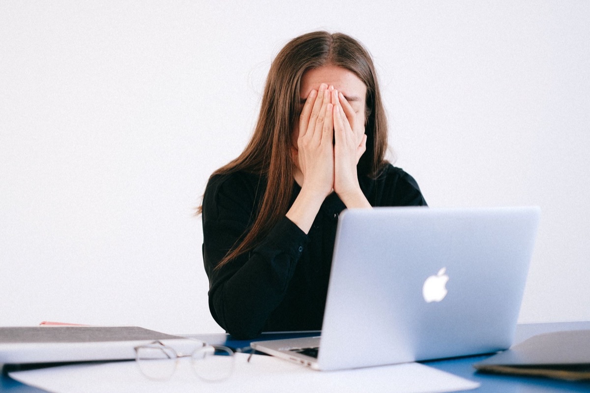 Femme assise à son bureau, l'air fatiguée et stressée, une main sur le front devant un ordinateur portable