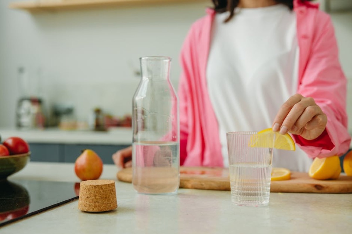 Femme buvant un verre d'eau citronnée dans une cuisine baignée de lumière naturelle