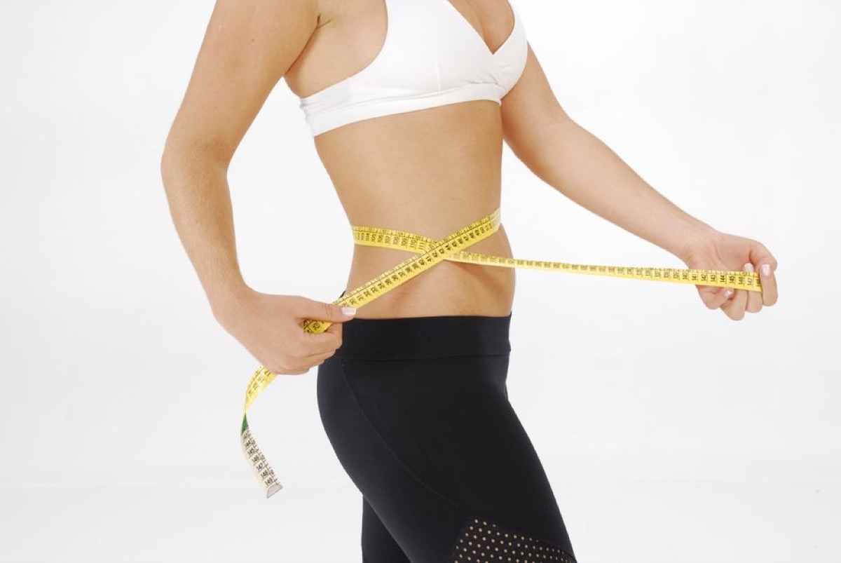 Femme souriante mesurant son tour de taille avec un mètre ruban devant une fenêtre lumineuse