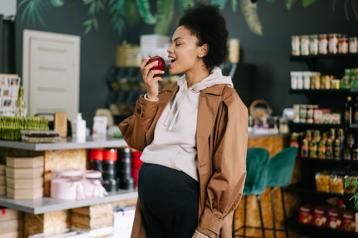 Femme enceinte souriante croquant une pomme en faisant ses courses