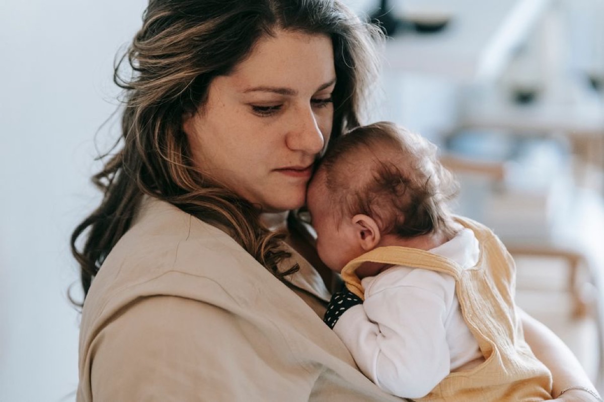 Jeune maman qui tient son nouveau-né contre elle, assise tranquillement chez elle