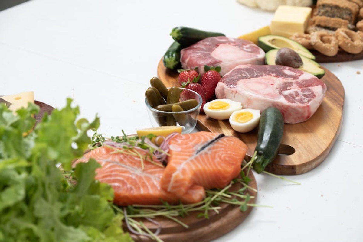 Ingrédients keto frais — saumon, viande, légumes verts — disposés sur une planche en bois