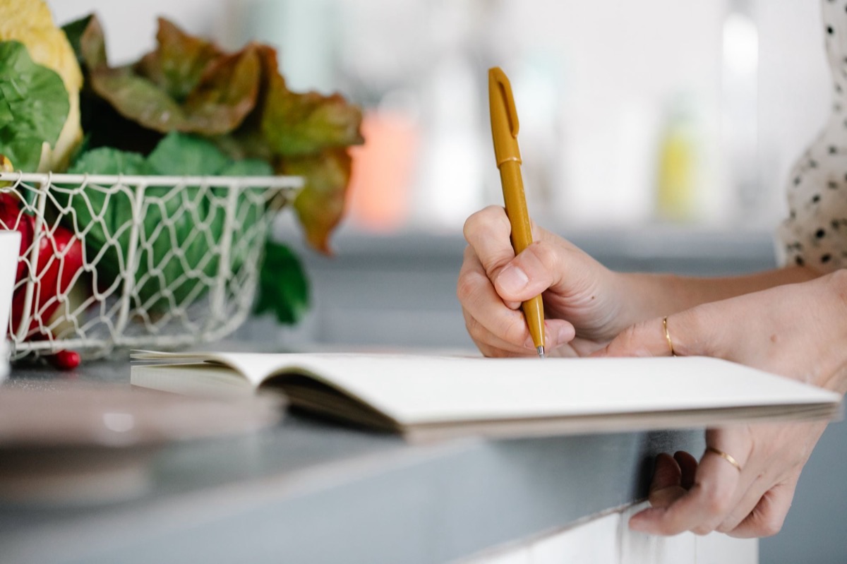 Carnet de suivi alimentaire ouvert sur une table de cuisine, à côté d'un bol de légumes frais et d'une tasse de café